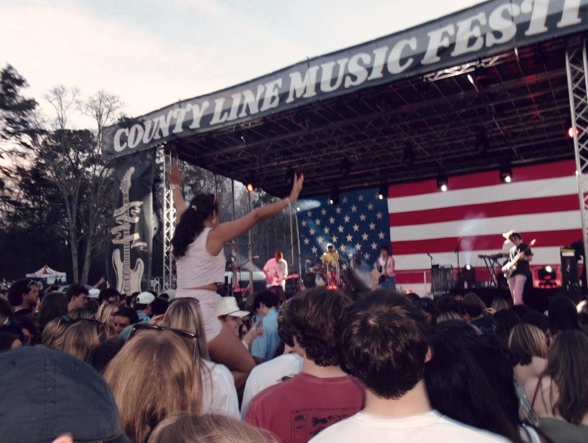 The County Line Music Festival arch over the stage, a flag behind the band and the crowd watching from the field.