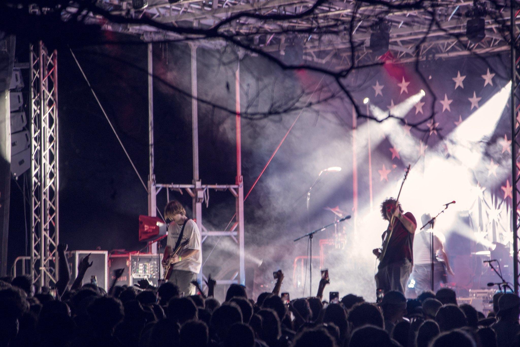 A night stage seen through bare trees, the crowd gathered below in silhouette.