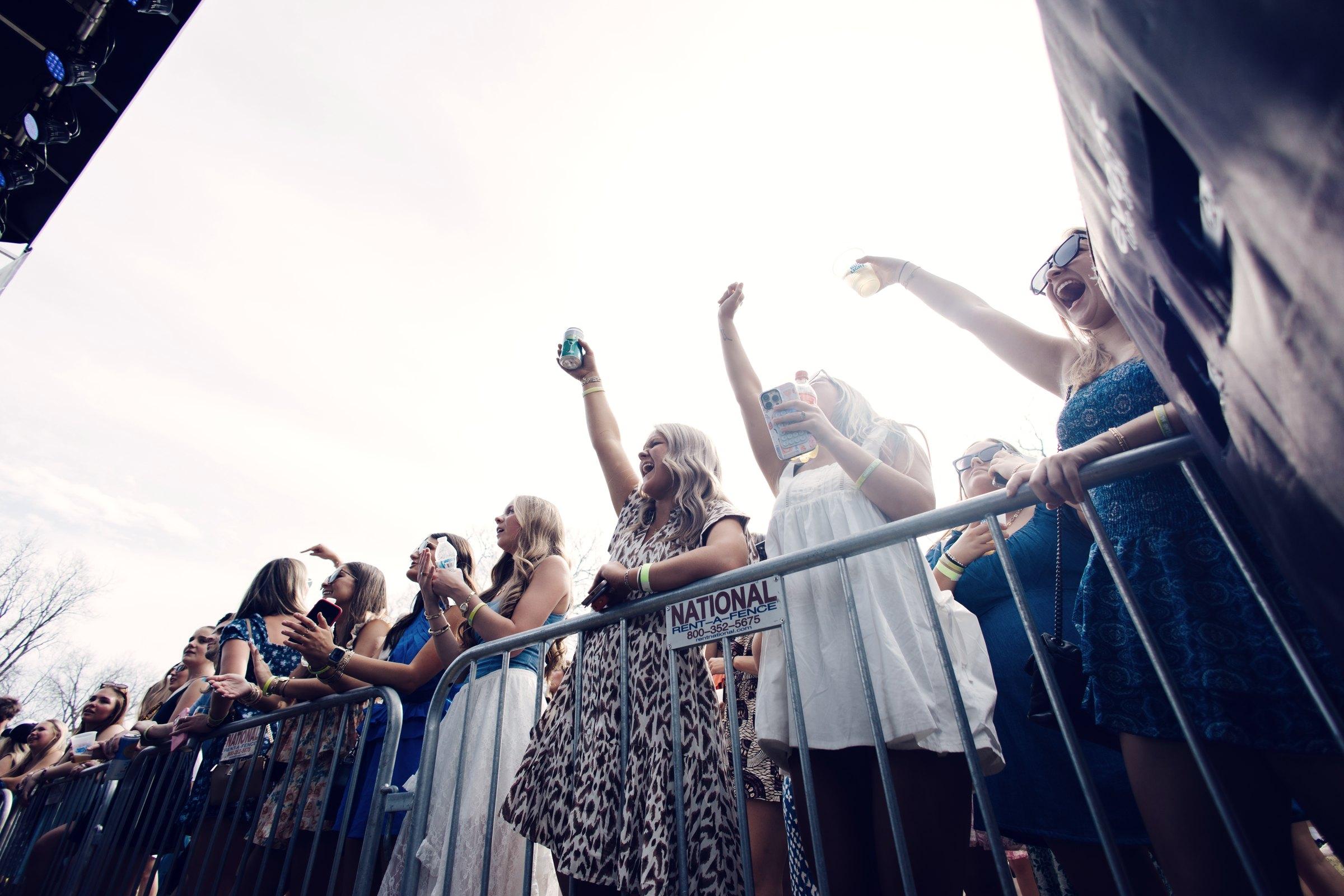 The front row at the barricade, arms up, photographed from below against an open sky.