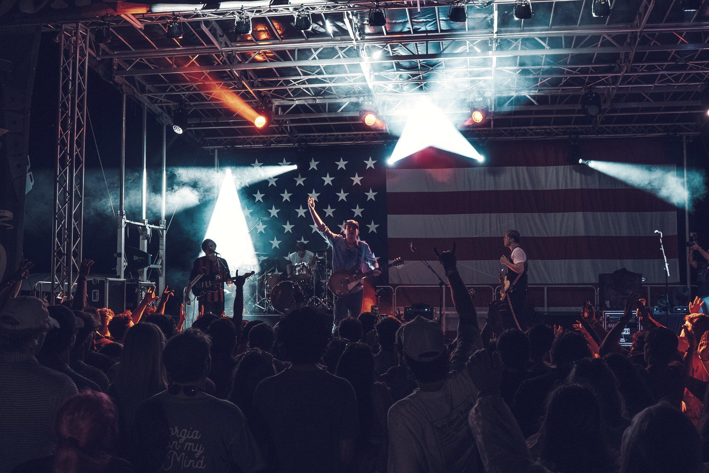 Beams cutting over a night stage and the silhouetted crowd standing in front of it.