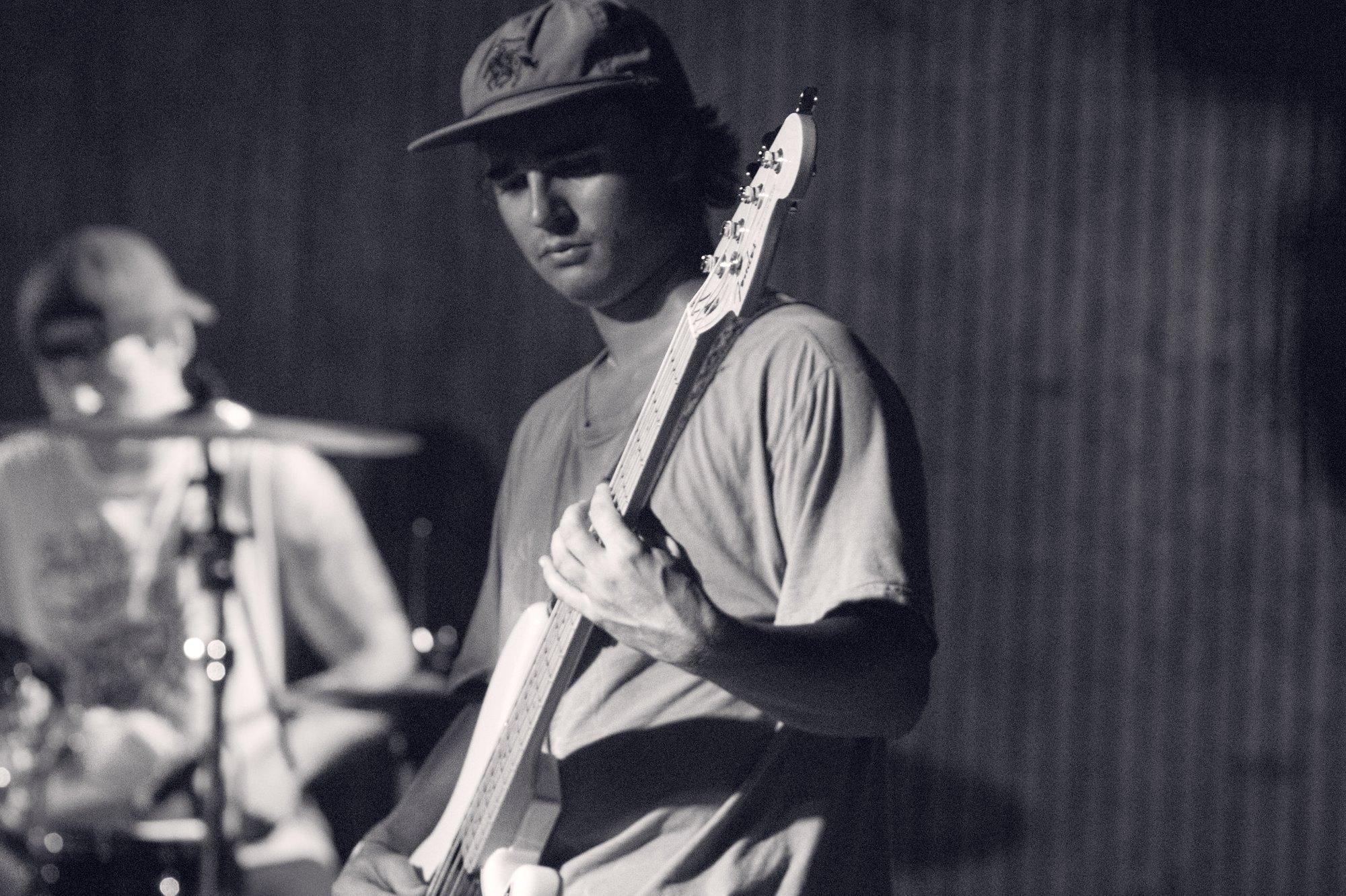 A bass player photographed in black and white, half-lit against a dark stage.