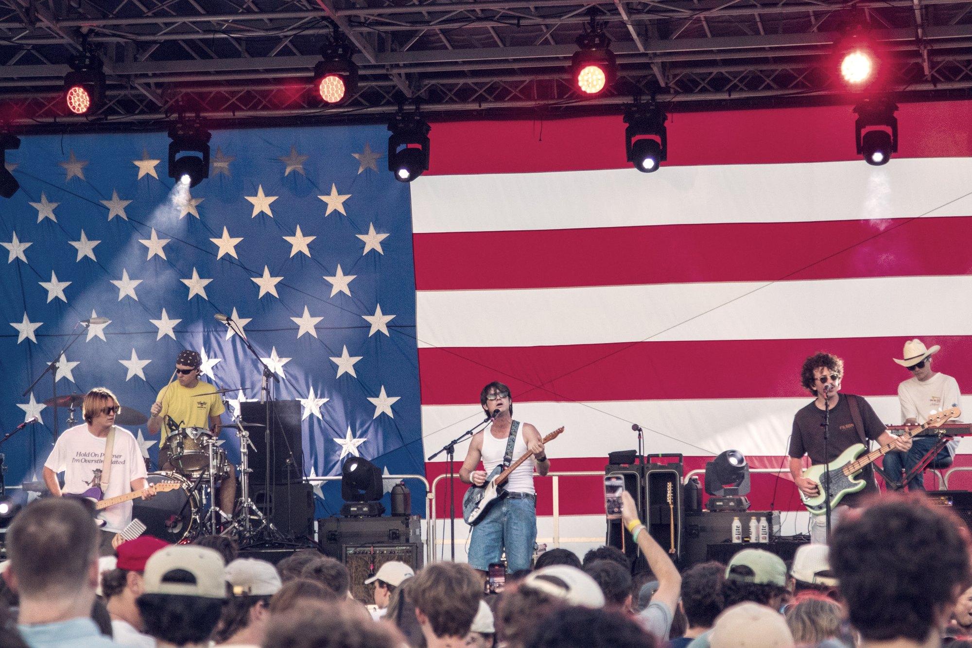 A night stage under a hung flag, the crowd gathered in silhouette below it.
